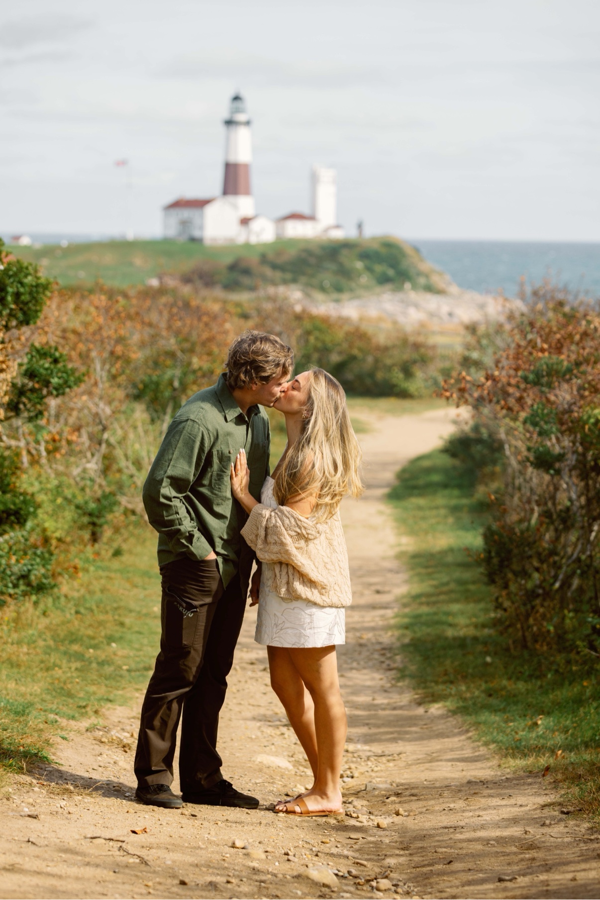 Surprise proposal at Montauk Lighthouse, Long Island — a couple kissing on the path just after the question