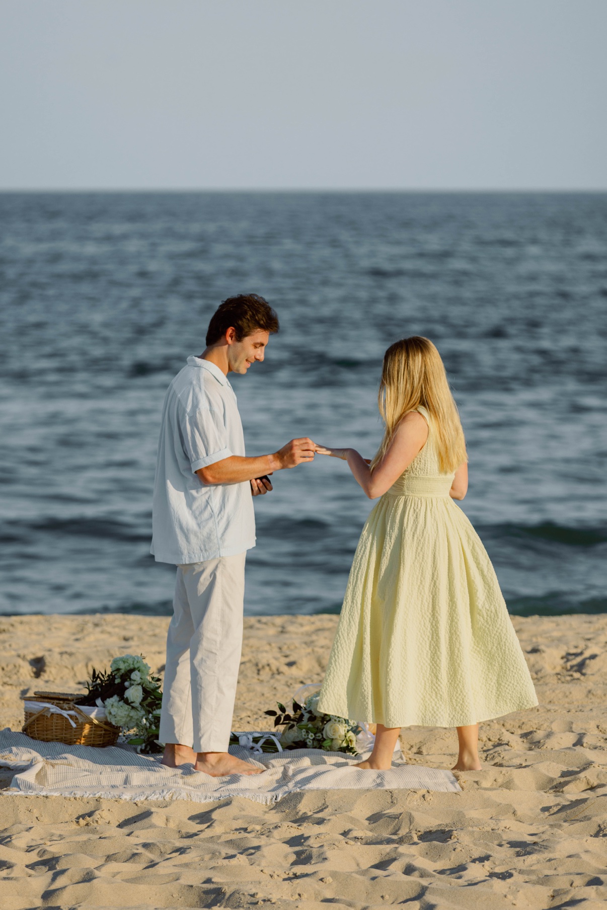 Slipping the engagement ring onto her hand during a beach proposal on Long Island