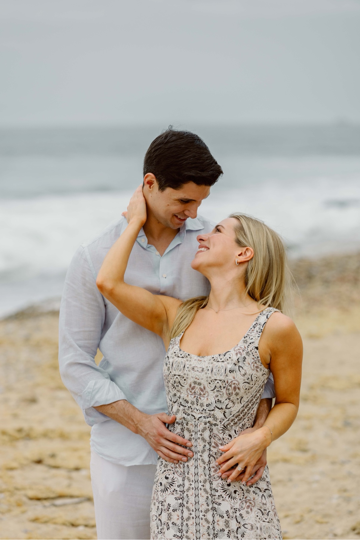 Engagement photos at Montauk Lighthouse, Long Island — a newly engaged couple embracing on the beach with the ocean behind them