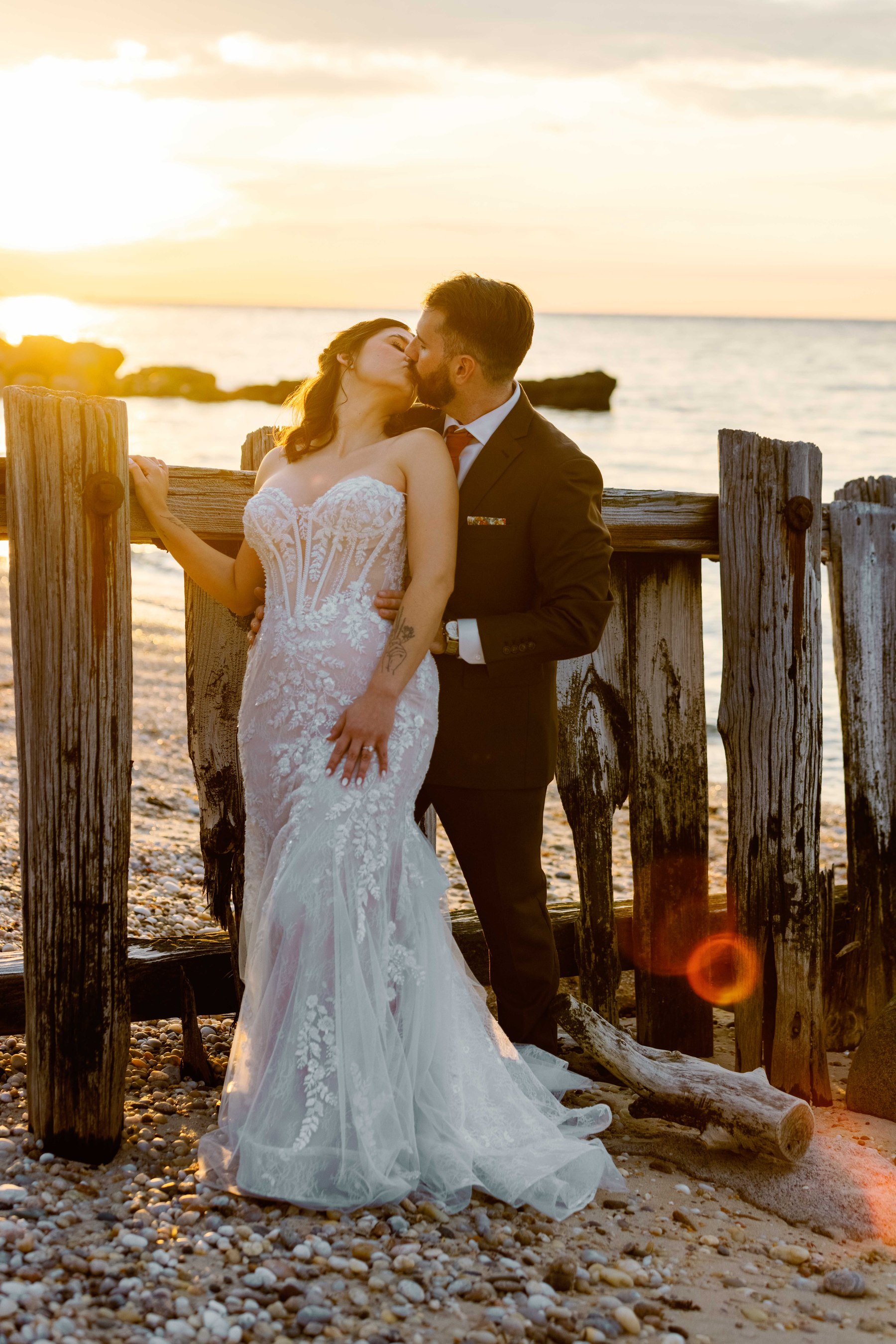 Newlyweds kissing beside the water at golden hour