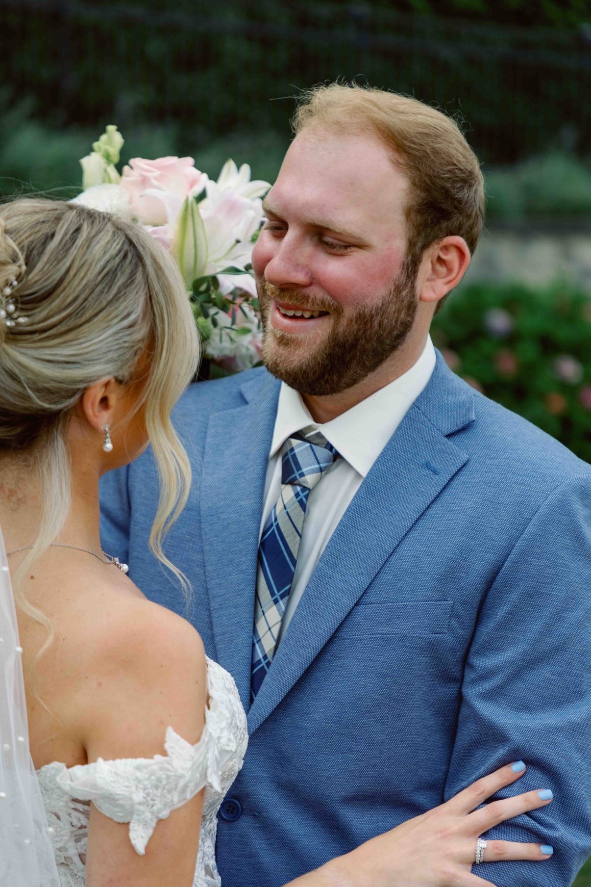 The groom smiling as he looks at the bride, her bouquet between them at The Muses