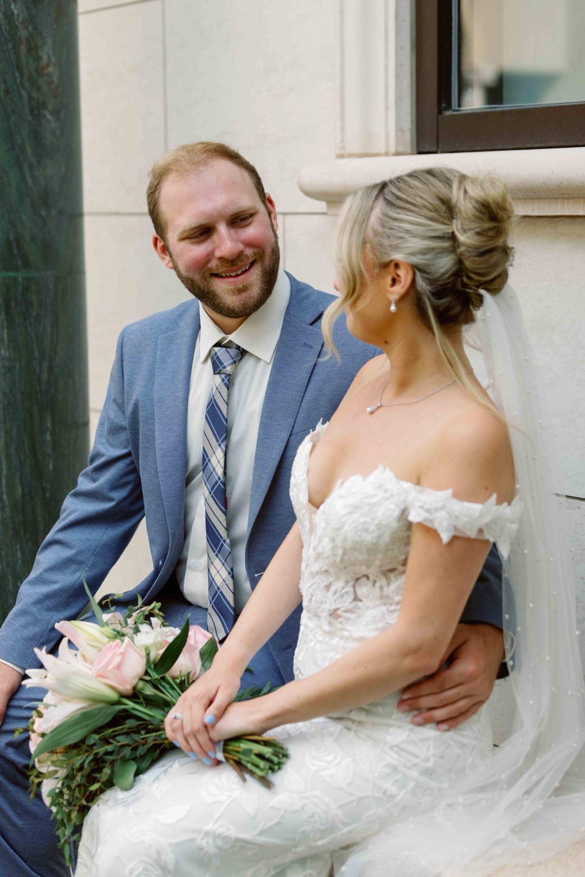 Bride and groom laughing together beside a green marble column at The Muses