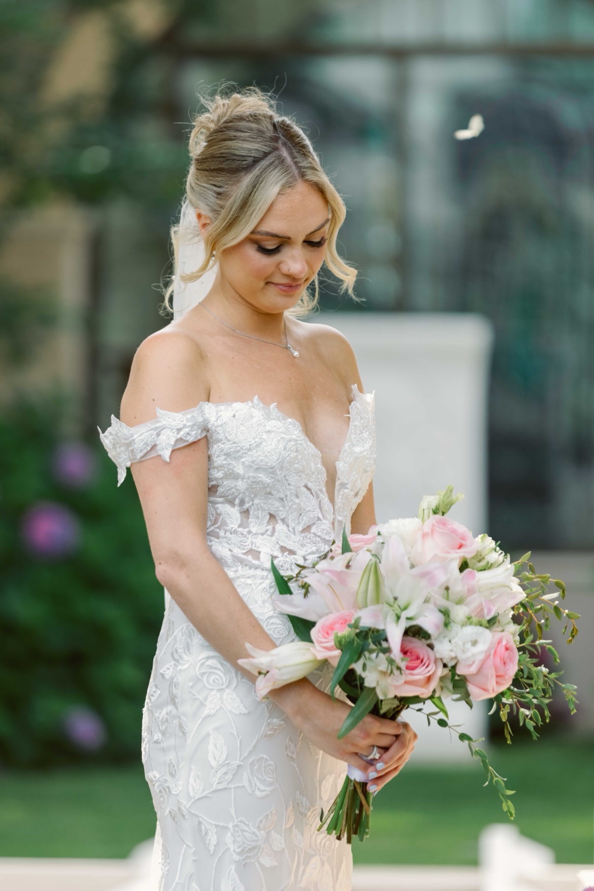 The bride holding her bouquet with her eyes lowered in the gardens at The Muses