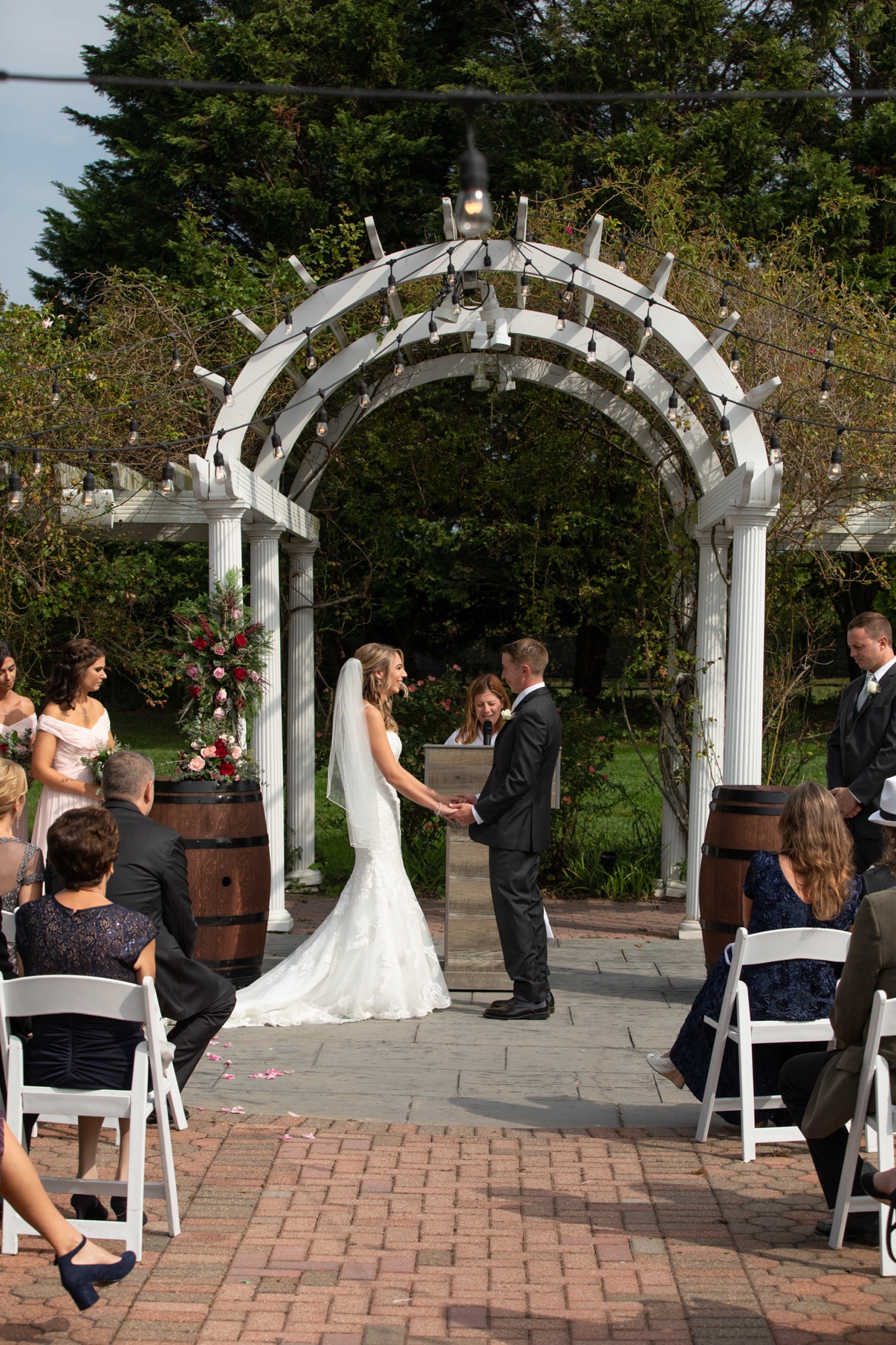 Bride and groom holding hands during their outdoor ceremony beneath a white pergola and string lights at a North Fork vineyard — Long Island wedding photographer