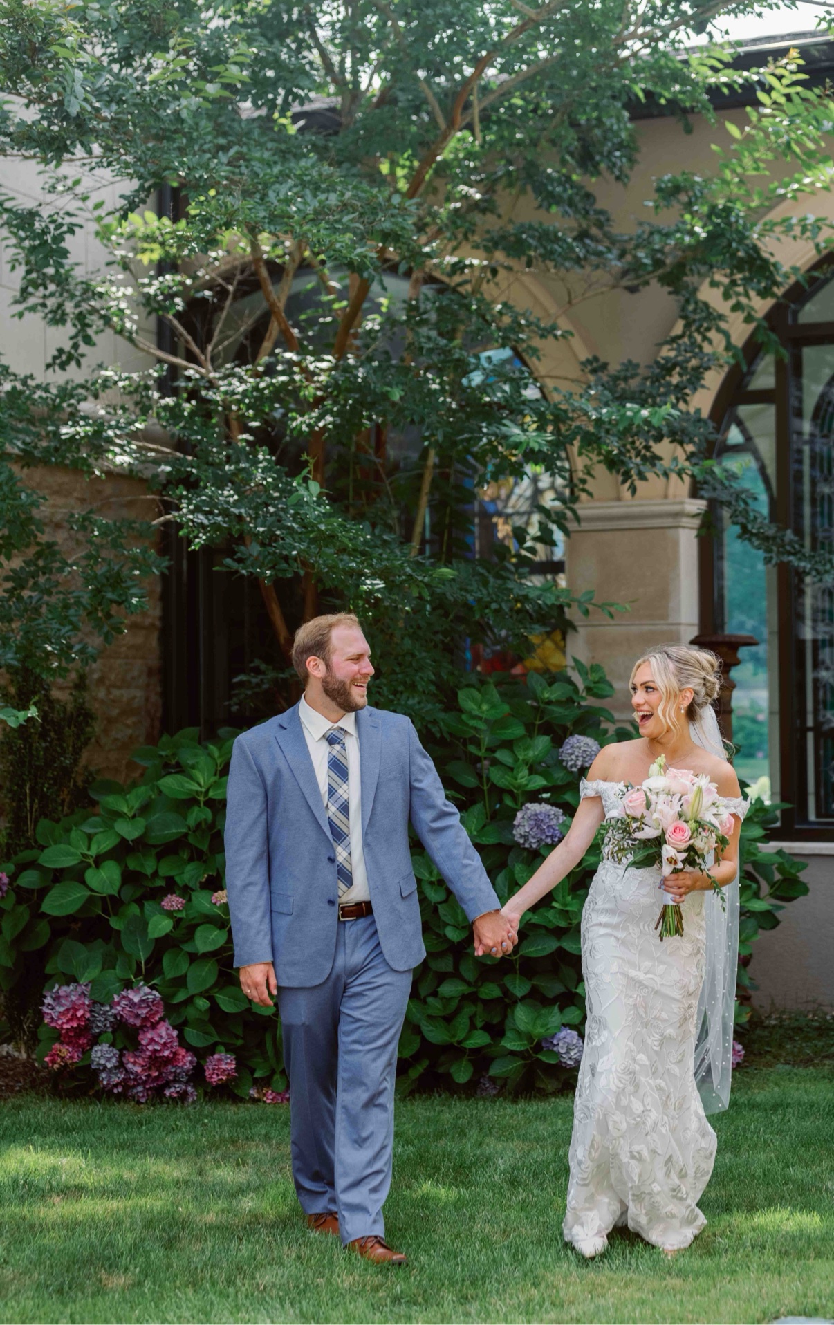 Bride and groom laughing as they walk hand in hand through the garden