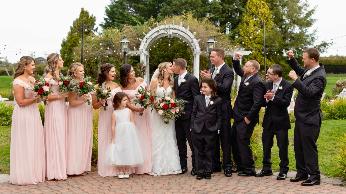 The wedding party gathered around the couple beneath the pergola at The Vineyards at Aquebogue