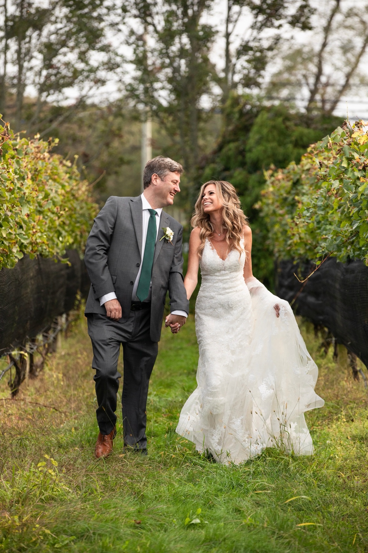 Newlyweds laughing as they walk hand in hand between the vineyard rows at The Vineyards at Aquebogue
